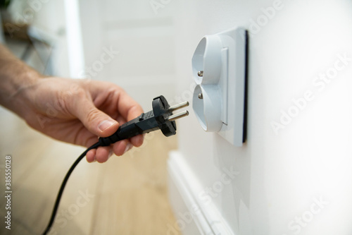 Inserting the plug into an electric socket in a bright interior, focus and close-up on a socket.