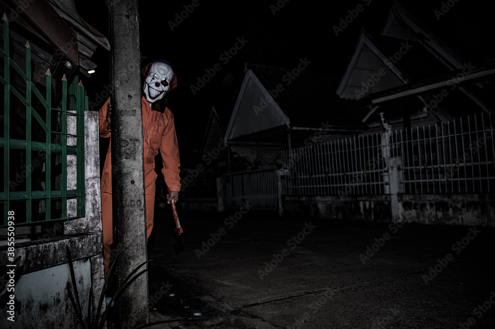 Asian handsome man wear clown mask with weapon at the night scene,Halloween festival concept,Horror scary photo of a killer in orange cloth