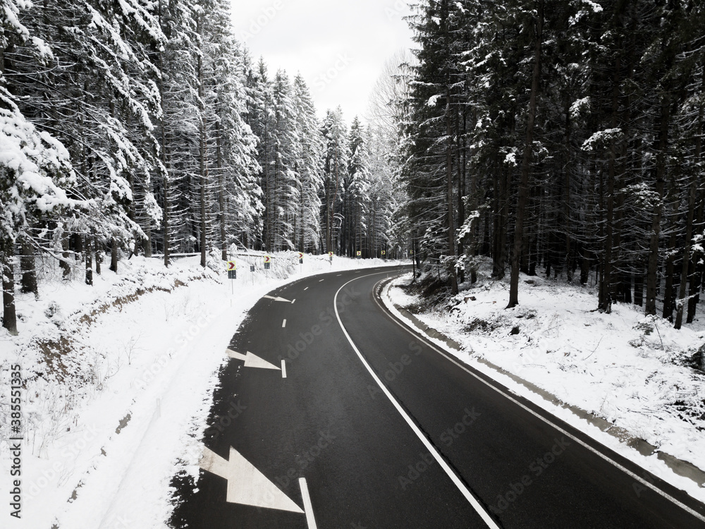 Fototapeta premium Winding road through the forest, from high mountain pass, in winter time. Aerial view by drone. Romania
