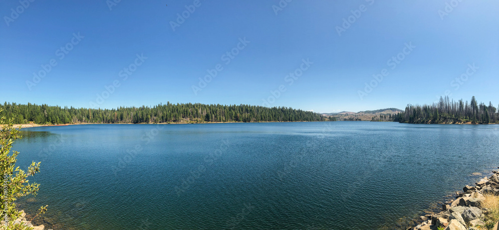 Photo of landscape with lake and blue sky surrounded of hills and forests