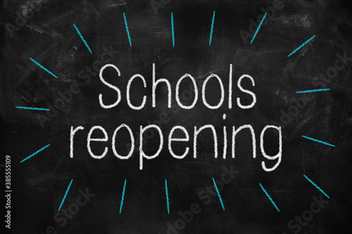 Schools reopening written with white and blue chalk on blackboard