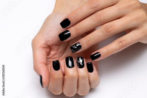 Design of nails for Halloween. Black manicure with a silver nail on short square nails close-up on a white background. Gel manicure.