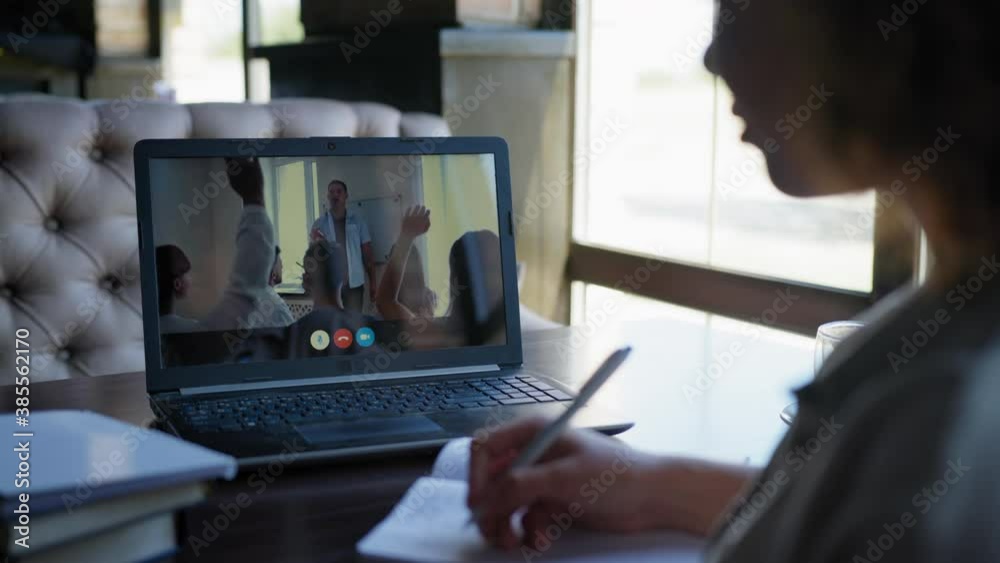online webinar, young female student undergoes remote training via video communication on laptop raises hand and answers question by making notes in notebook sitting at table by window online webinar, young female student undergoes remote training via video communication on laptop raises hand and answers question by making notes in notebook sitting at table by window
