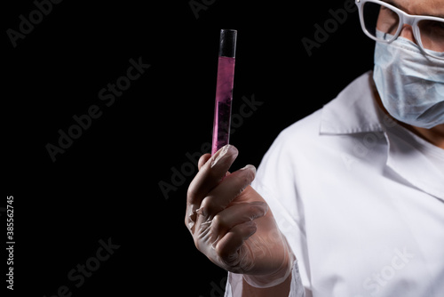 laboratory assistant in a medical mask and in a white coat with a liquid in a flask and a chemical on a black background