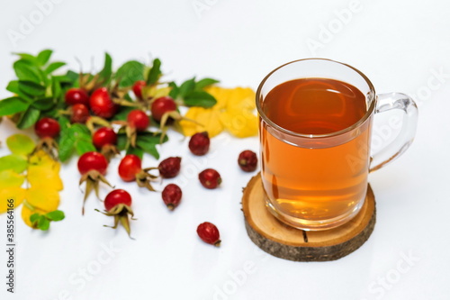 healthy rosehip tea in a glass Cup on a wooden saw, next to dry and fresh rosehip berries on a white surface