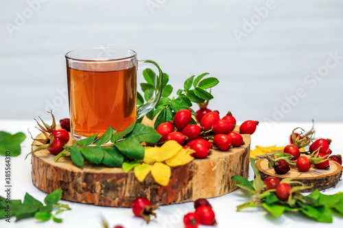 healthy rosehip tea in a glass Cup on a wooden saw, next to dry and fresh rosehip berries on a white surface