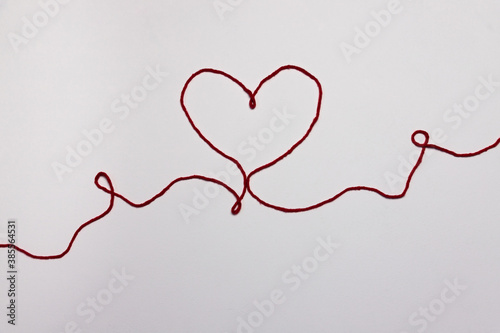 Heart shape made with red thread. Valentine's day, love message on light pink white background