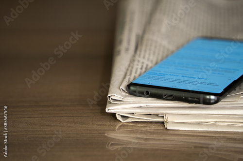 Closeup of color stacked newspapers on a wooden table background with mobile phone.
