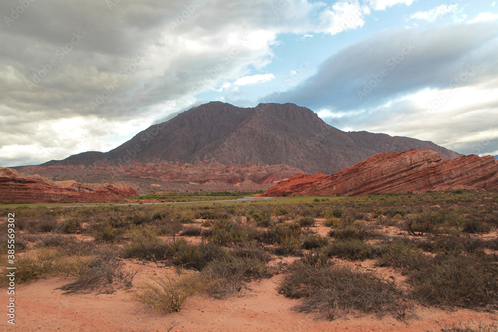 Desert landscape. View of the arid valley, sand, shrubs, red sandstone, rocky formations and mountains. 
