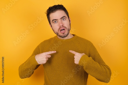 Photo of embarrassed Young man wearing casual sweater and over isolated yellow background indicates at hisself with puzzled expression, being shocked photo