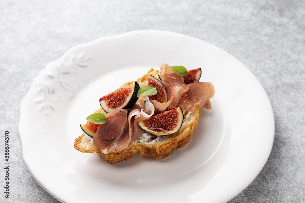 Croissant with figs, jamon, curd cheese and basil on a vintage plate Croissant with figs, jamon, curd cheese and basil on a vintage plate