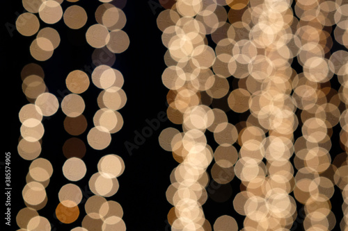 Defocused luminous garland. Gold Christmas garland texture. Abstract bokeh festoon on dark background. Christmas lights