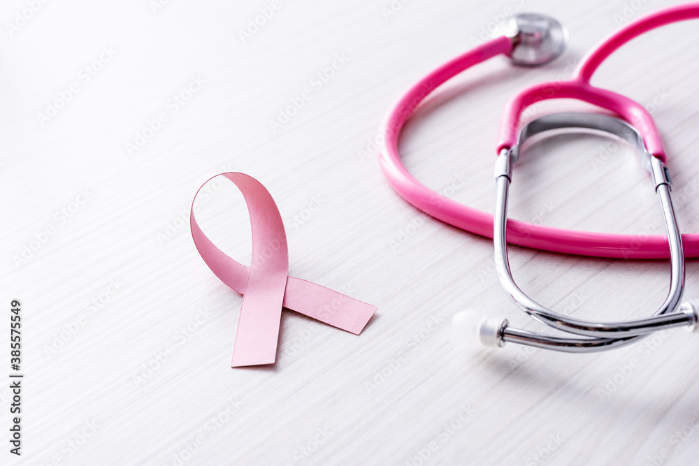 Pink ribbon of breast cancer awareness near stethoscope on white wooden background