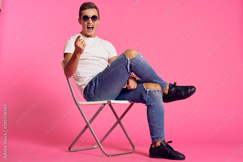 A man sits on a chair in a white t-shirt and jeans modern style pink isolated background A man sits on a chair in a white t-shirt and jeans modern style pink isolated background