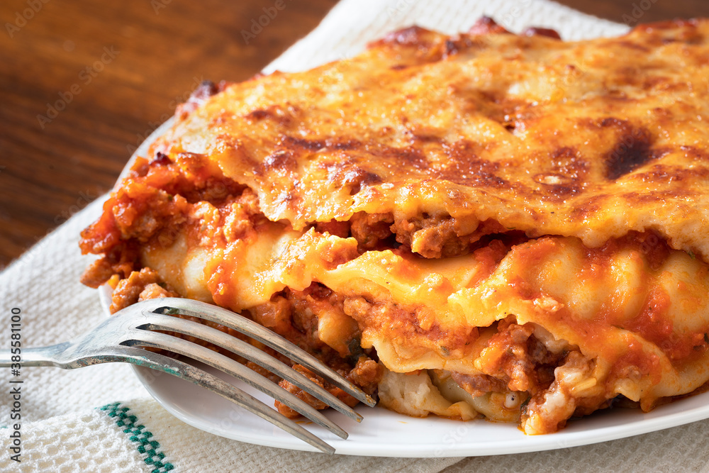 Close up of a portion of traditional italian lasagna with meat in a plate with a fork.