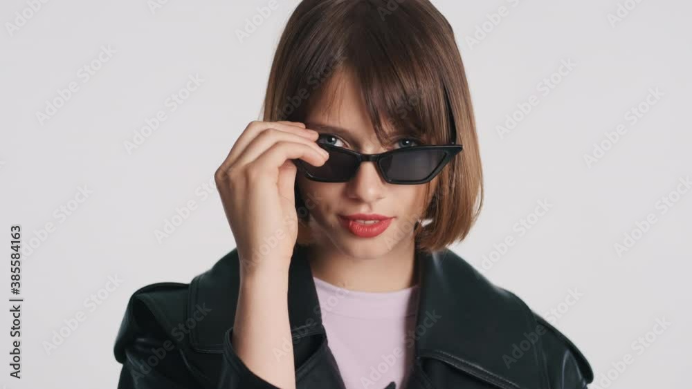 Attractive fashion brunette girl with bob hair putting on sunglasses over white background. Stylish model posing in studio Attractive fashion brunette girl with bob hair putting on sunglasses over white background. Stylish model posing in studio