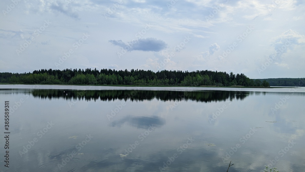 landscape of a blue lake and sky with white clouds on a forest background and also their reflection in the water during the daytime in summer