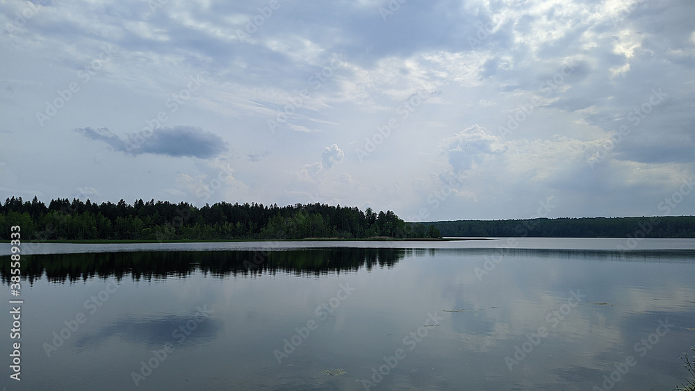 landscape of a blue lake and sky with white clouds on a forest background and also their reflection in the water during the daytime in summer