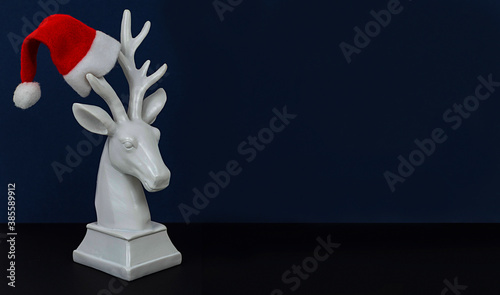 white deer in Santa hat on dark blue background, minimal creative concept of Christmas and New Year
