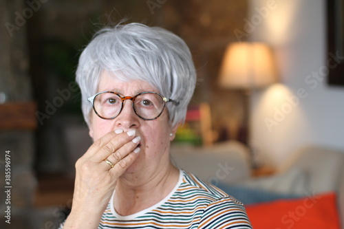 Worried senior woman covering mouth with hand 