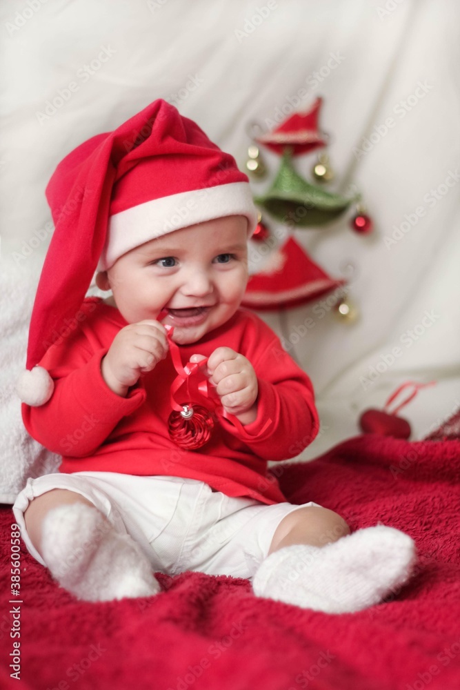 A beautiful little child is celebrating Christmas. New year holiday. Baby in a Christmas costume is happy sitting on the floor A beautiful little child is celebrating Christmas. New year holiday. Baby in a Christmas costume is happy sitting on the floor