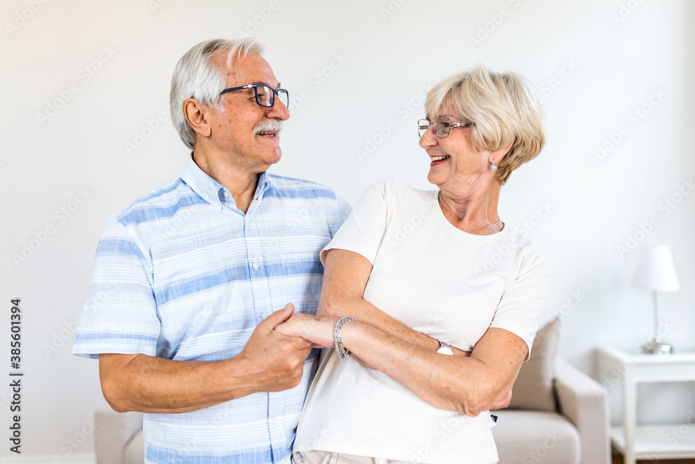 Obraz premium Joyful active old retired romantic couple dancing laughing in living room, happy middle aged wife and elder husband having fun at home, smiling senior family grandparents relaxing bonding together