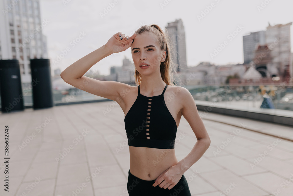 Confident fitness woman in sport bra looking away while training outside on city background