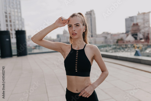 Confident fitness woman in sport bra looking away while training outside on city background © PhotoBook