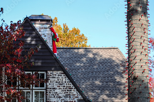 Closeup of house with Christms lights on roof and tree and deflated blow-up santa hanging from chimney photo