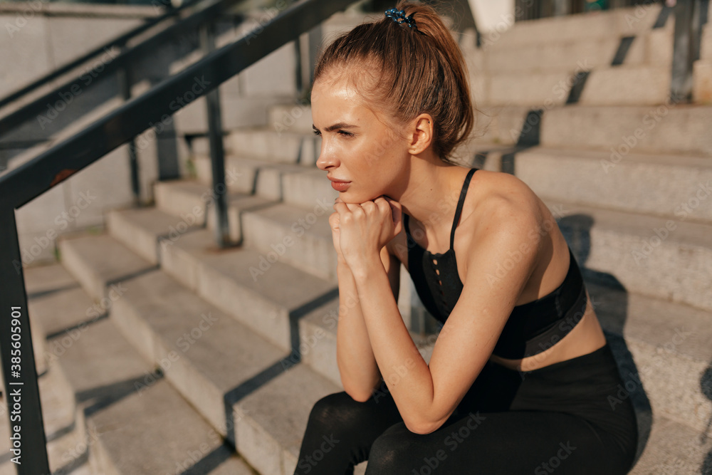European young woman in sport black uniform sitting on concrete staircase. Young woman with fit body running against grey background. Female model in sportswear exercising outdoors. European young woman in sport black uniform sitting on concrete staircase. Young woman with fit body running against grey background. Female model in sportswear exercising outdoors.
