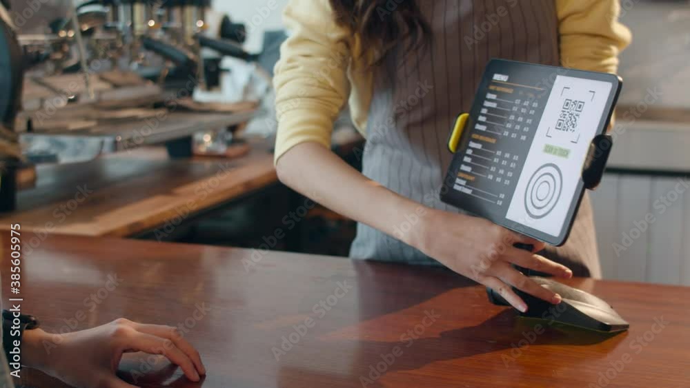 Young Asia female self service use mobile phone pay contactless with tablet at cafe restaurant. Girl barista talking receive orders from customer at bar counter in coffee shop. Owner small business.