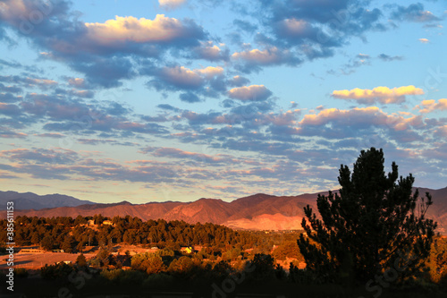 Orange golden hour sunshine on the foothills of the Rock Mountains in Colorado Springs USA with puffy clouds framed by shadowy trees and shadows in the foreground photo