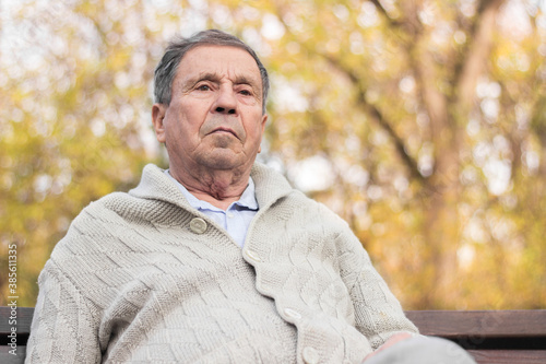 Portrait of a pensive senior man sitting on the bench, in the public park, outdoors. Old man relaxing outdoors and looking away. Portrait of elderly man enjoying retirement