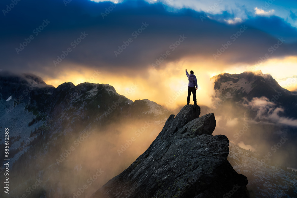 Fantasy Adventure Composite with a Man on top of a Mountain Cliff with Dramatic Landscape in Background during Sunset or Sunrise. Landscape from British Columbia, Canada.