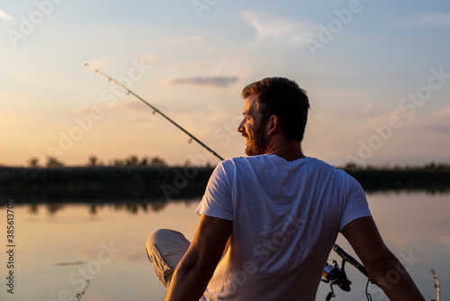 Fotobehang Back view of fisherman sitting at the river dock and fishing at sunset