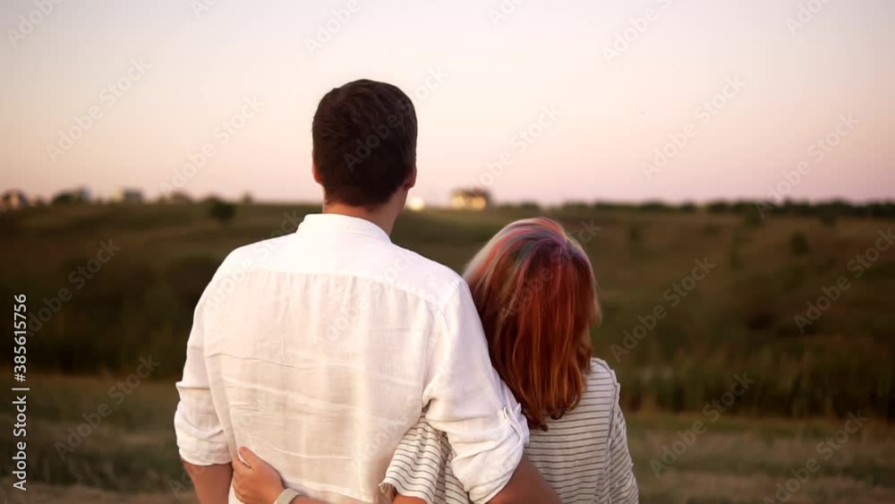 Man and woman are standing in field and looking at skyline discussing something. Young caucasian couple is hugging. Lady points at something and addresses to boyfriend. Theme of love and relationship. Man and woman are standing in field and looking at skyline discussing something. Young caucasian couple is hugging. Lady points at something and addresses to boyfriend. Theme of love and relationship.