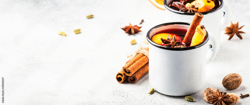 Mulled wine in white metal mugs with cinnamon, spices and orange on gray background, traditional drink on winter holiday. Copy space - obrazy, fototapety, plakaty 