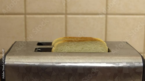 A woman puts bread in a toaster. The bread is fried. Breakfast food is being prepared. Electrical appliance in the kitchen