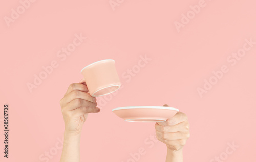 Hands holding up a cup and saucer on a soft pink background, with copy spacce photo