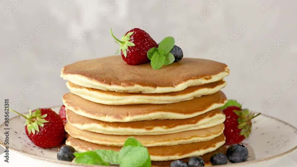 Pancake with strawberry, blueberry and mint in ceramic dish on rotated on light table, close up. Pancake with strawberry, blueberry and mint in ceramic dish on rotated on light table, close up.