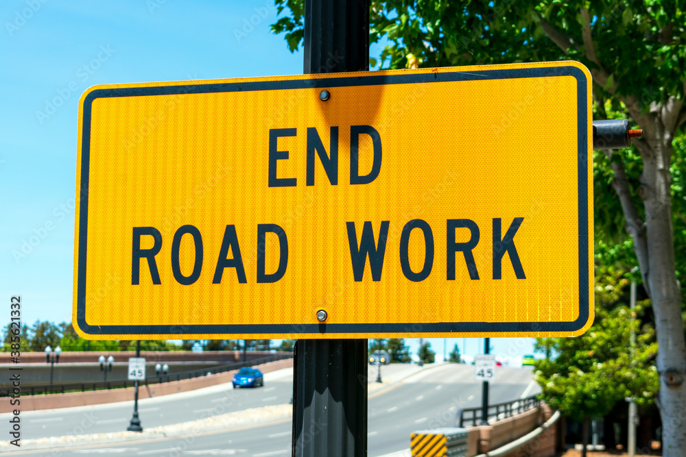 End Road Work traffic sign. Background wide urban street with a few cars End Road Work traffic sign. Background wide urban street with a few cars
