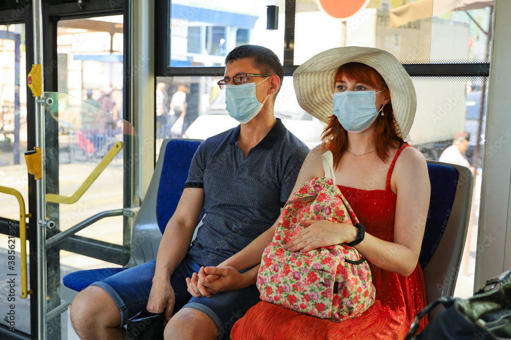 Young couple wearing medical face masks are sitting in public transport and holding hands on summer day. Safety rules during pandemic