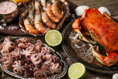 Assorted of seafood on rustic wooden table. Top view of tiger shrimps, cooked crab and baby octopuses served with lime and seashells. Concept of delicious food from the sea or ocean.