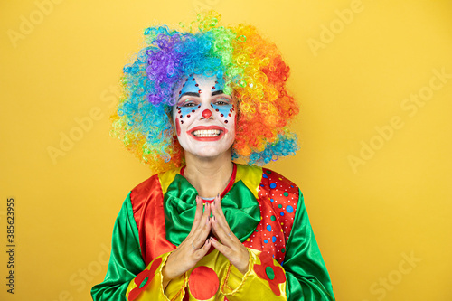 Clown standing over yellow insolated yellow background with Hands together and fingers crossed smiling relaxed and cheerful. Success and optimistic