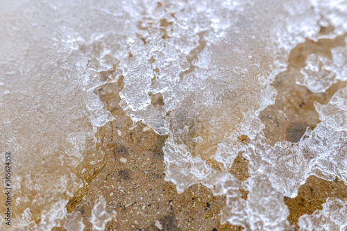 Detail of a thin layer of ice melting on the ground, winter background.