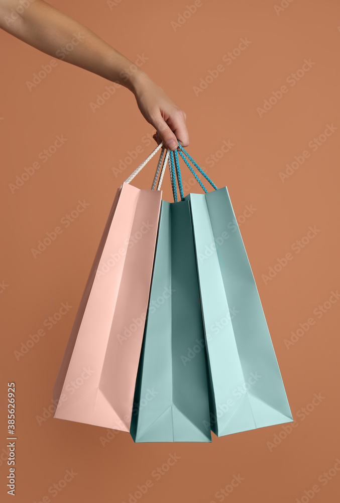Woman holding paper shopping bags on light brown background, closeup