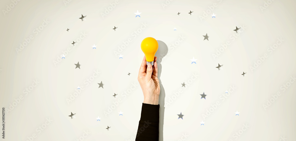 Fototapeta premium Person holding a yellow light bulb with silver shiny stars