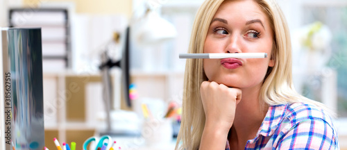 Young woman holding a pen above lips in an office