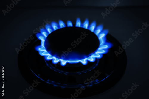 Gas burner of modern stove with burning blue flame at night