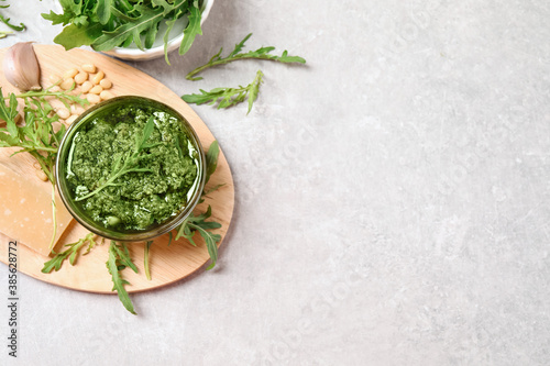 Bowl of tasty arugula pesto and ingredients on light table, flat lay. Space for text